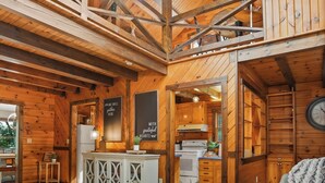 A spacious wooden interior with a high ceiling, a dining area, and a kitchen visible through an open doorway.