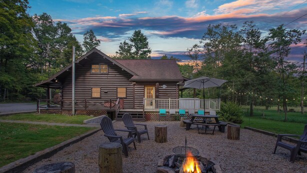 A rustic log cabin with a deck, outdoor seating, and a fire pit.