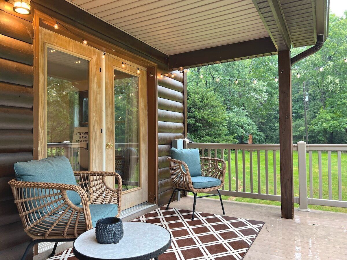 A covered porch with wicker chairs and a table, overlooking a grassy area.
