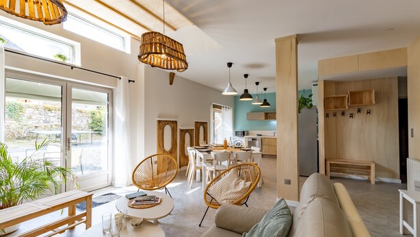 A modern living room with a sofa, chairs, a dining table, and a kitchen area in the background.