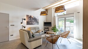 A modern living room with a sofa, two chairs, a coffee table, a TV, and a large window.