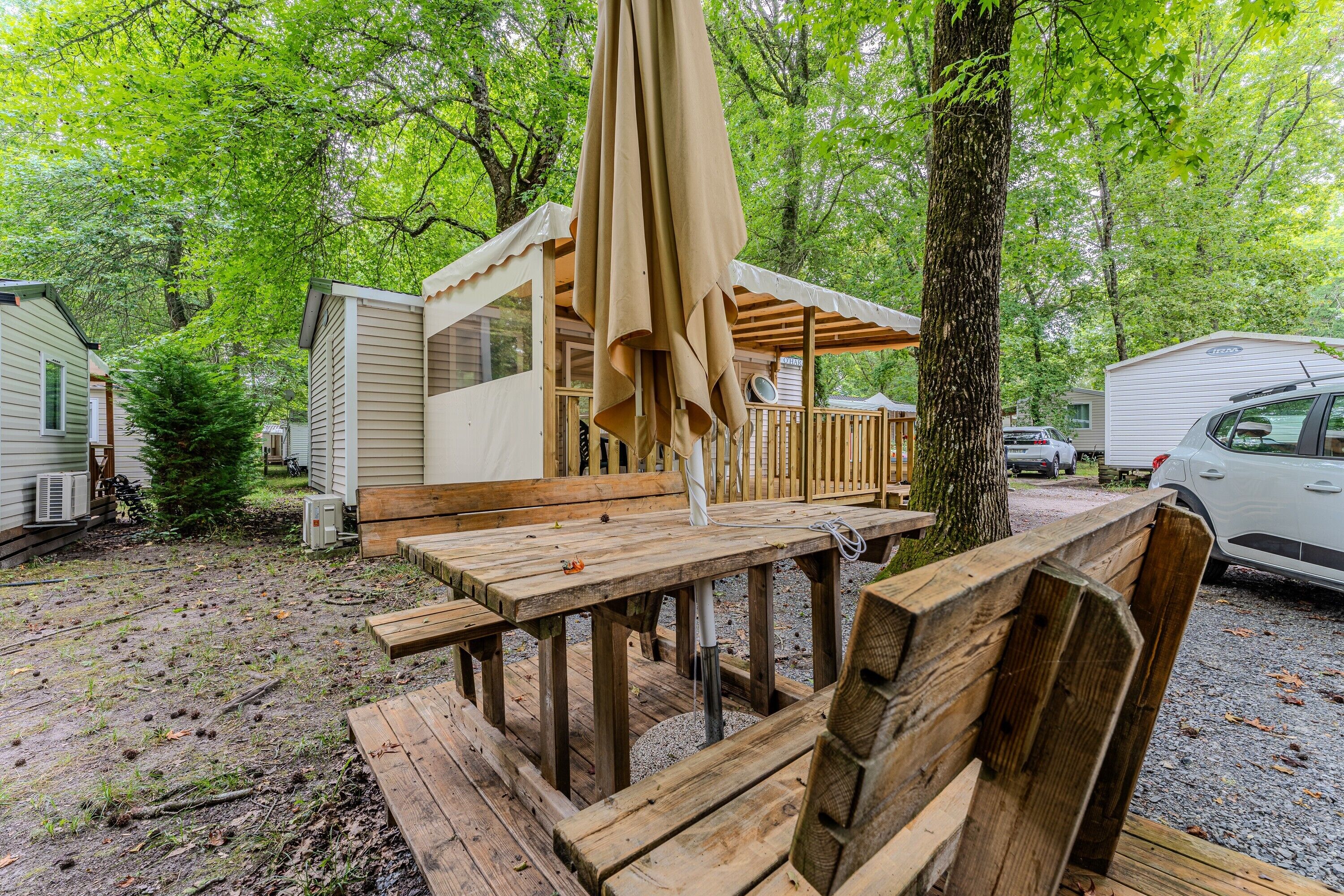 A wooden deck with a table and chairs, surrounded by trees and a covered area with a beige canopy.