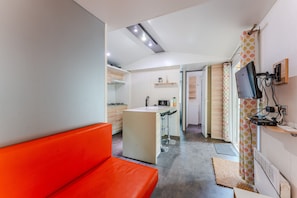 Eine moderne Küche mit einer zentralen Kochinsel, einem Essbereich mit Barhocker und einem leuchtend orangefarbenen Sofa.
