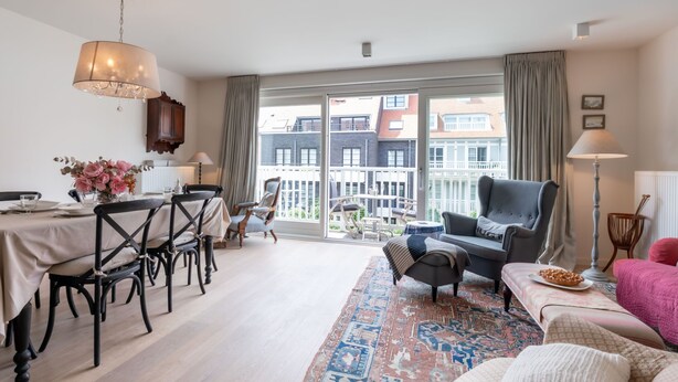 A spacious living area with a dining table, chairs, a sofa, and a balcony with a view of buildings.