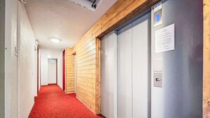 Un pasillo con alfombra roja, paneles de madera en una pared y una puerta de ascensor gris con un cartel.