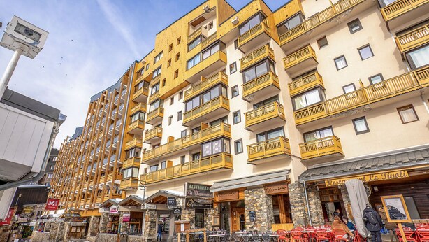 Un hotel de varios pisos con balcones, mobiliario exterior y un restaurante.
