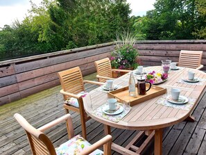Une terrasse en bois avec une table ronde prévue pour accueillir six personnes, entourée de chaises en bois.