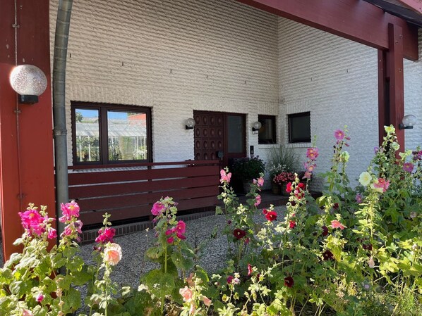 Un bâtiment à la façade rouge, un banc en bois et un jardin où poussent différentes sortes de fleurs.