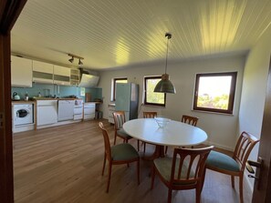 Uma cozinha moderna com armários de madeira, uma área de jantar com mesa e cadeiras redondas, e uma janela grande que traz luz natural.