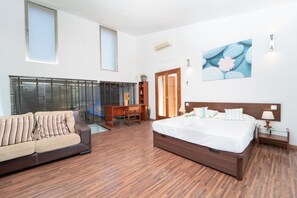 A modern hotel room with a wooden floor, a large bed, a sofa, a desk, and a window with blinds. - Villa can Costa in Alcudia by Home Villas 360 (Alcúdia)
