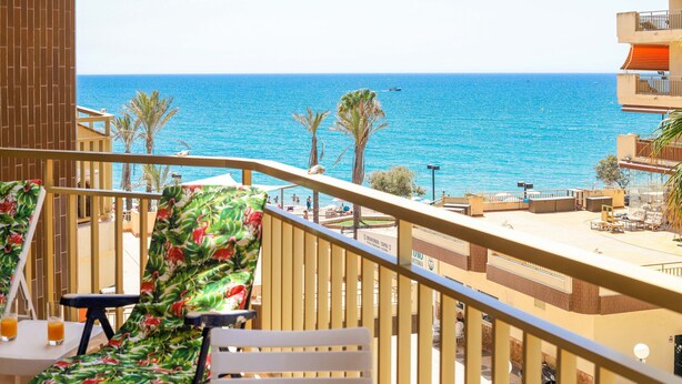 Un balcón con vista al mar, una mesa, una silla y una barandilla.