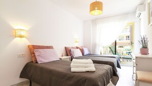 Habitación de hotel con dos camas, un escritorio pequeño, una planta en maceta y un balcón con vistas.