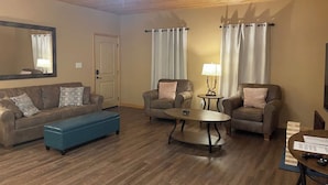 A living room with a wooden ceiling, a ceiling fan, a large mirror, two sofas, a coffee table, and a blue ottoman.