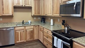 A kitchen with wooden cabinets, a stainless steel microwave, a black stove, and a granite countertop.