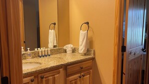 A bathroom with a granite countertop, wooden cabinets, a large mirror, and a towel rack.