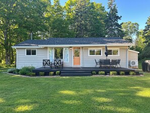 A single-story house with a covered porch, a front door, and a small patio area with outdoor furniture. - Family friendly cottage, centrally located, w/large yard- minutes from the water (Summerside)