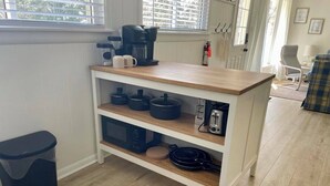 Una cucina con piano di lavoro in legno, due ripiani con pentole, una macchina da caffè e un cestino.