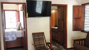Una habitación con una cama, una silla de madera, un televisor montado en la pared y un ventilador de techo.