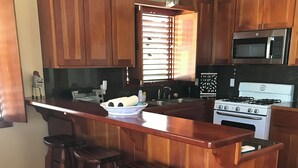 Una cocina con armarios de madera, un microondas de acero inoxidable, una estufa blanca y una zona de bar con taburetes.