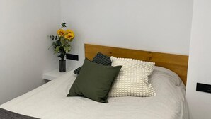 A neatly arranged bedroom with a bed, pillows, a bedside table, and a vase with flowers. - WELCS ESTUDIO 172 EMP con piscina comunitaria (Rosas / Roses)
