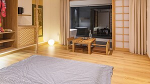 A modern hotel room with a wooden floor, a large window with a view of the city, a wooden table with a chair, and a bed with a striped blanket. - Hajime Homestay (Hue)