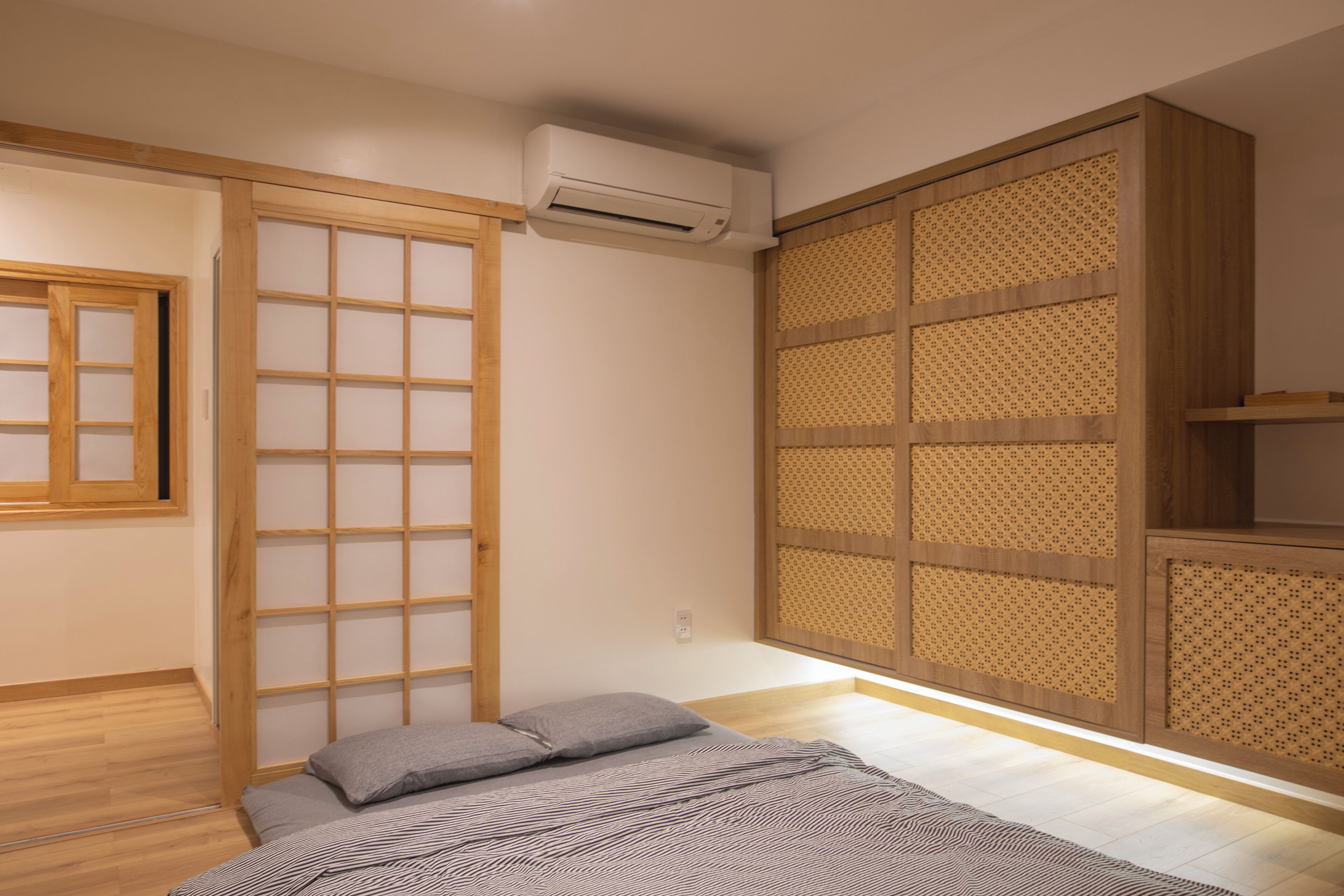 Una habitación con una cama, una puerta corredera, un equipo de aire acondicionado y un panel de madera con diseño de celosía.