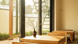 A traditional Japanese-style room with tatami flooring, wooden furniture, and large windows offering a view of the outdoors. - Hajime Homestay (Hue)