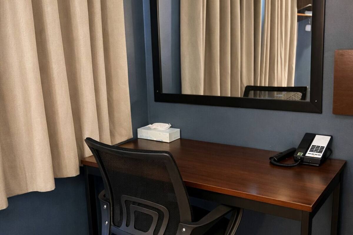 Ein Hotelzimmer mit einem Holztisch, einem schwarzen Bürostuhl, einem Telefon und einem Spiegel an der Wand.