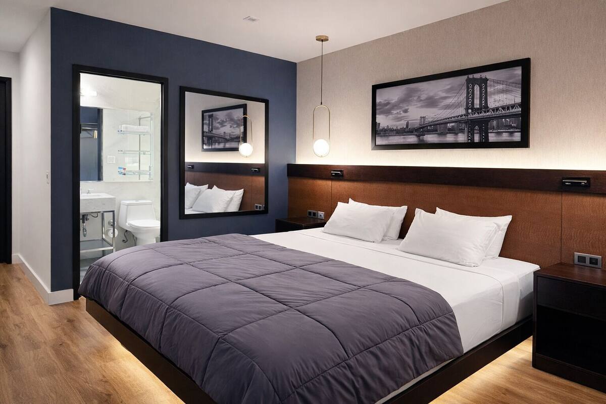 Ein modernes Hotelzimmer mit einem großen Bett, einem Nachttisch, einem Spiegel und einem Bild einer Brücke.