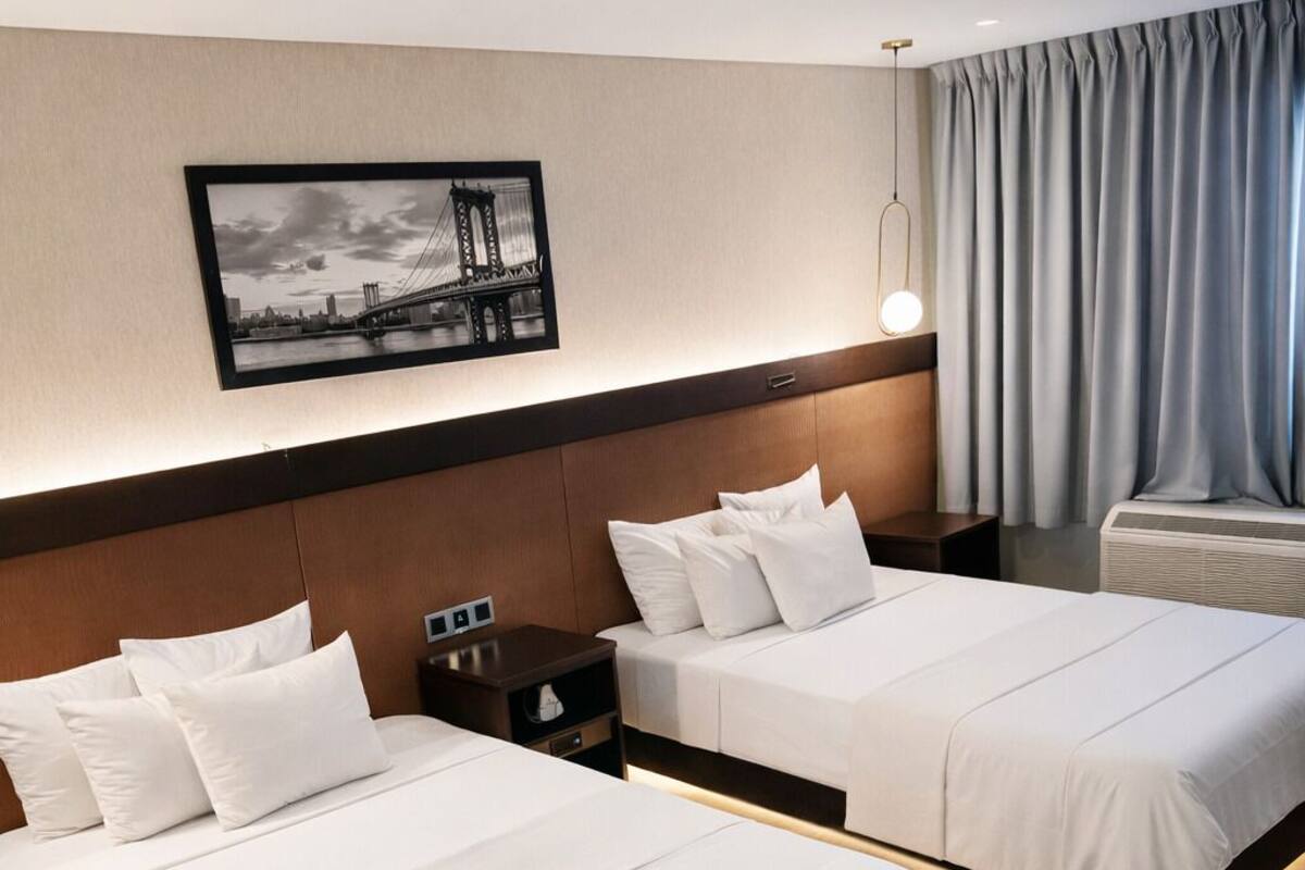 Ein Hotelzimmer mit zwei Betten, einem Nachttisch, einer Lampe und einem gerahmten Bild an der Wand.