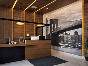 A reception area with a wooden reception desk, pendant lighting, and a large cityscape mural featuring a bridge. - Hotel Mirage Brooklyn  (Brooklyn)
