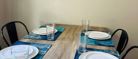 A dining table set with plates, glasses, and cutlery, with a blue placemat and a framed picture above.
