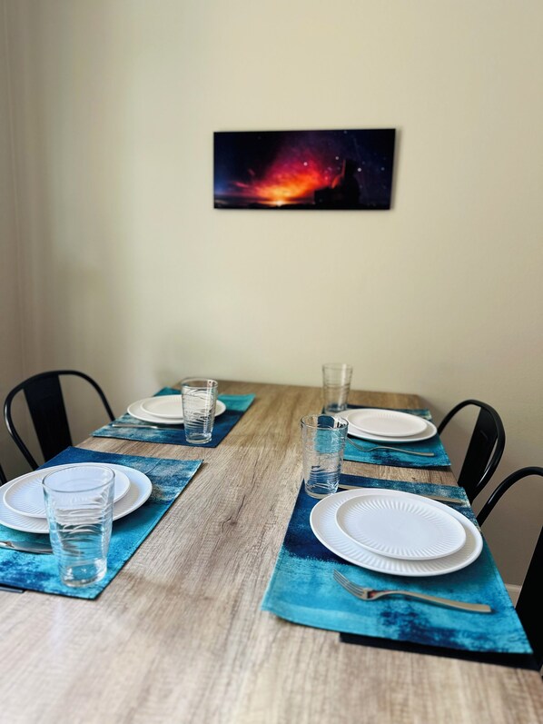 A dining table set with plates, glasses, and cutlery, with a blue placemat and a framed picture above. - Cozy 2-bedroom condo with WiFi, AC in-both bedrooms - Waikoloa Village (Waikoloa Village)