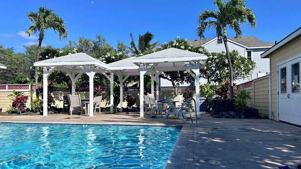 A swimming pool with two white gazebos, palm trees, and a house in the background. - Cozy 2-bedroom condo with WiFi, AC in-both bedrooms - Waikoloa Village (Waikoloa Village)