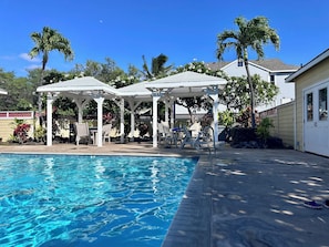 A swimming pool with two white gazebos, palm trees, and a house in the background. - Cozy 2-bedroom condo with WiFi, AC in-both bedrooms - Waikoloa Village (Waikoloa Village)
