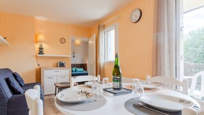 A well-lit dining area with a round table set for two, a bottle of wine, and a clock on the wall. - Fleur Marine by Interhome (Cabourg)