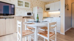 A compact kitchen with white cabinets, a microwave, and a dining area with a white table and chairs. - Fleur Marine by Interhome (Cabourg)