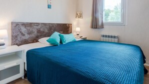 A bedroom with a bed, a nightstand, a lamp, a window with curtains, and a wall decoration. - Fleur Marine by Interhome (Cabourg)