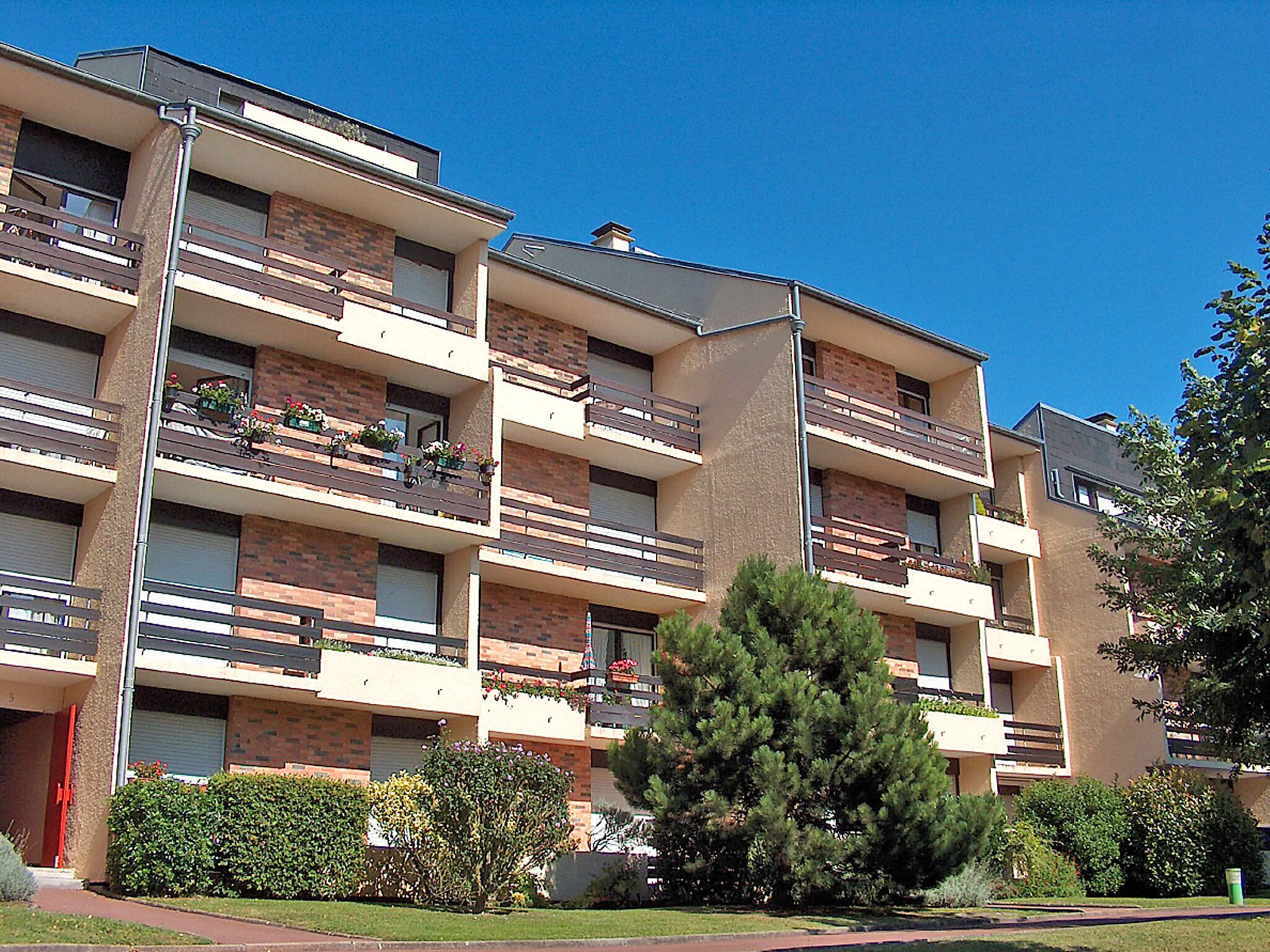 A multi-story residential building with balconies, brick facade, and a clear blue sky.