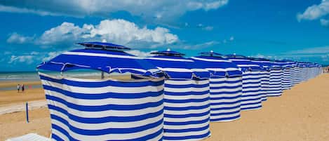 A row of striped beach umbrellas on a sandy beach.