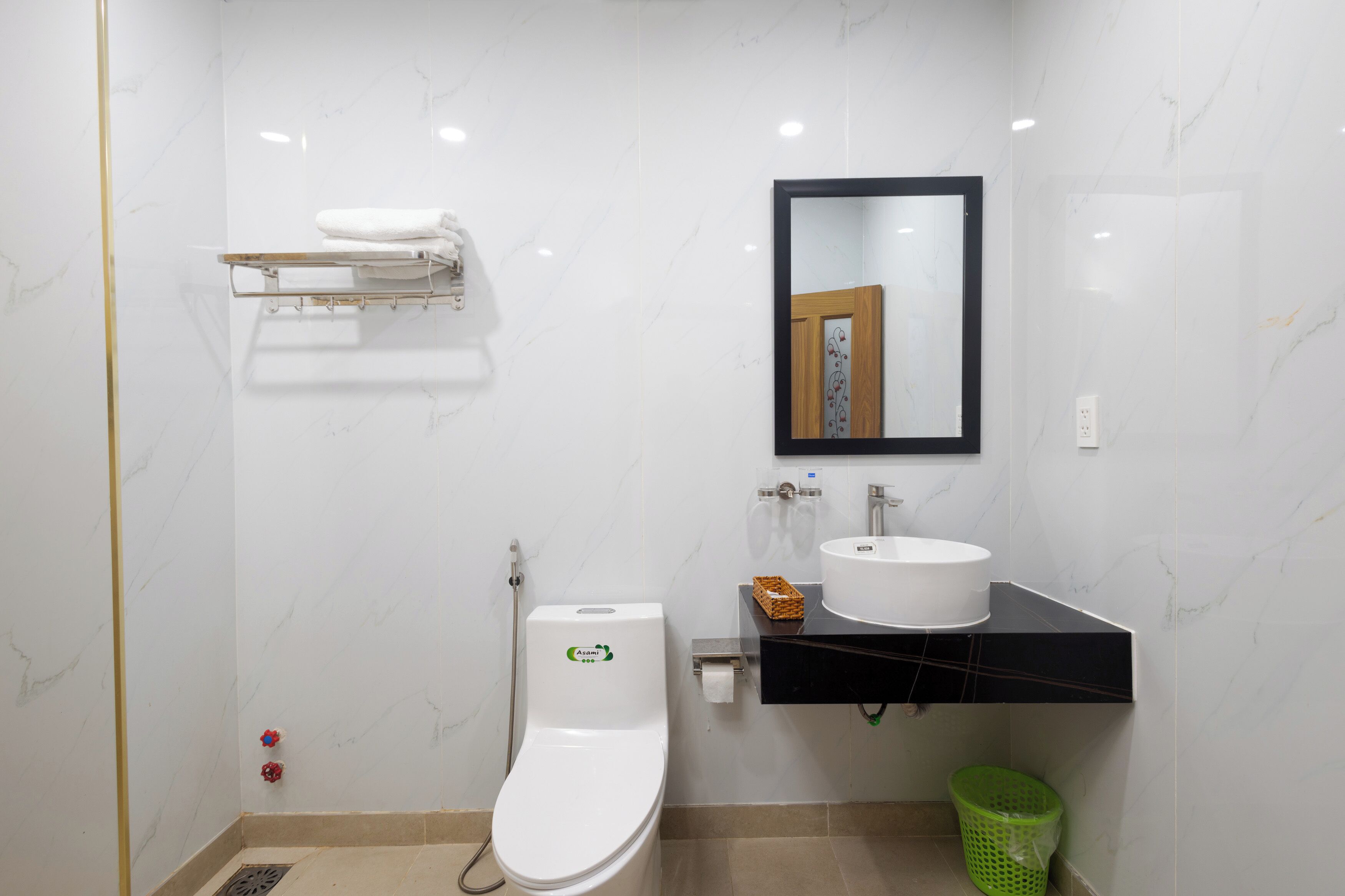 A bathroom with a toilet, sink, mirror, towel rack, and green trash bin.
