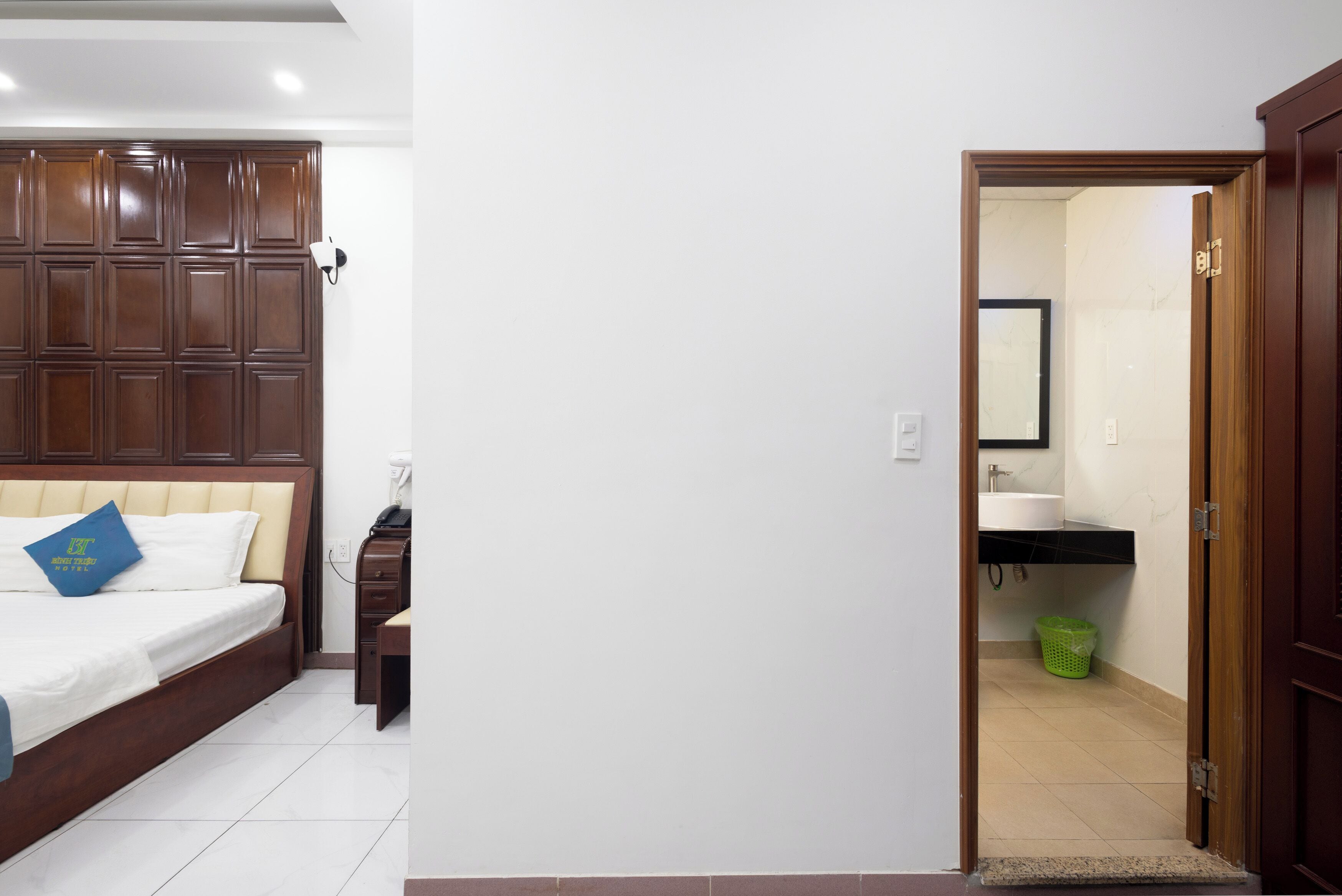 A bedroom with a wooden headboard, a bed with white bedding, a nightstand, and a green basket.