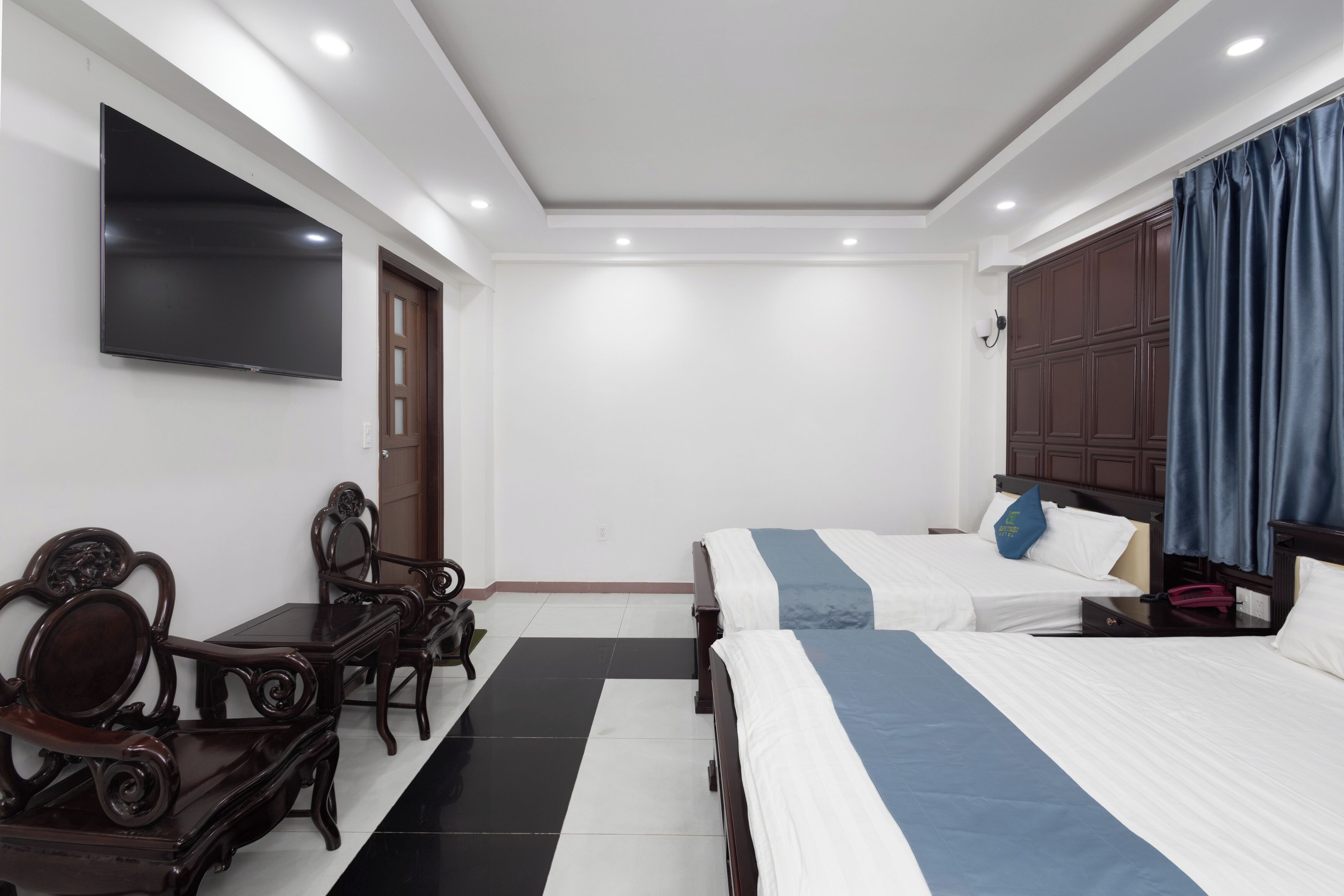 A hotel room with two beds, a TV mounted on the wall, a wooden desk, and a wardrobe.