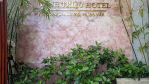 Az 1st Triệu Hotel külső megjelenése: márványburkolatos homlokzat és buja zöld növényzet.