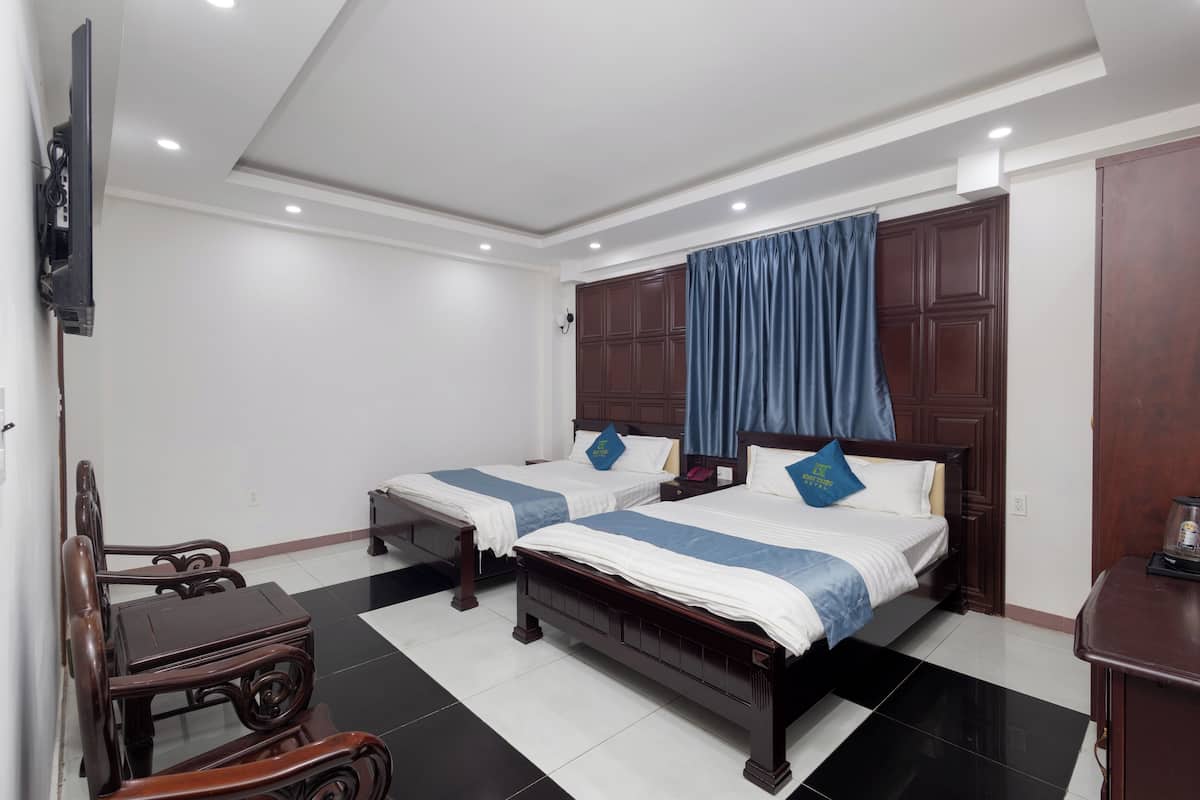 A hotel room with two beds, a TV mounted on the wall, a wooden chair, and a desk.