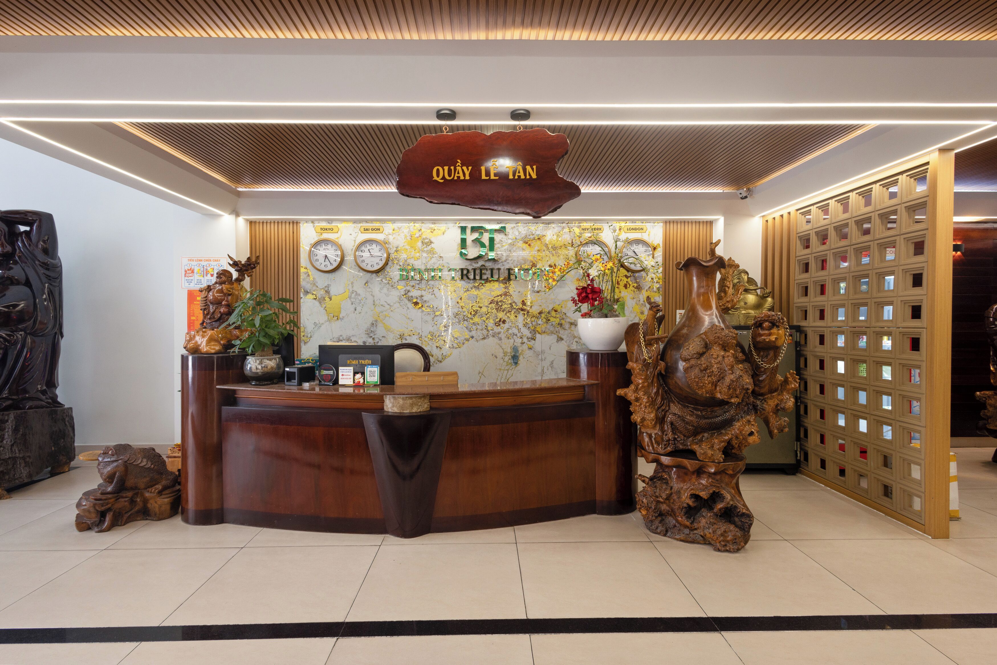 A reception desk with a wooden finish, a world map, clocks, and a sign above reading "QUÁY LÊ TÂN".