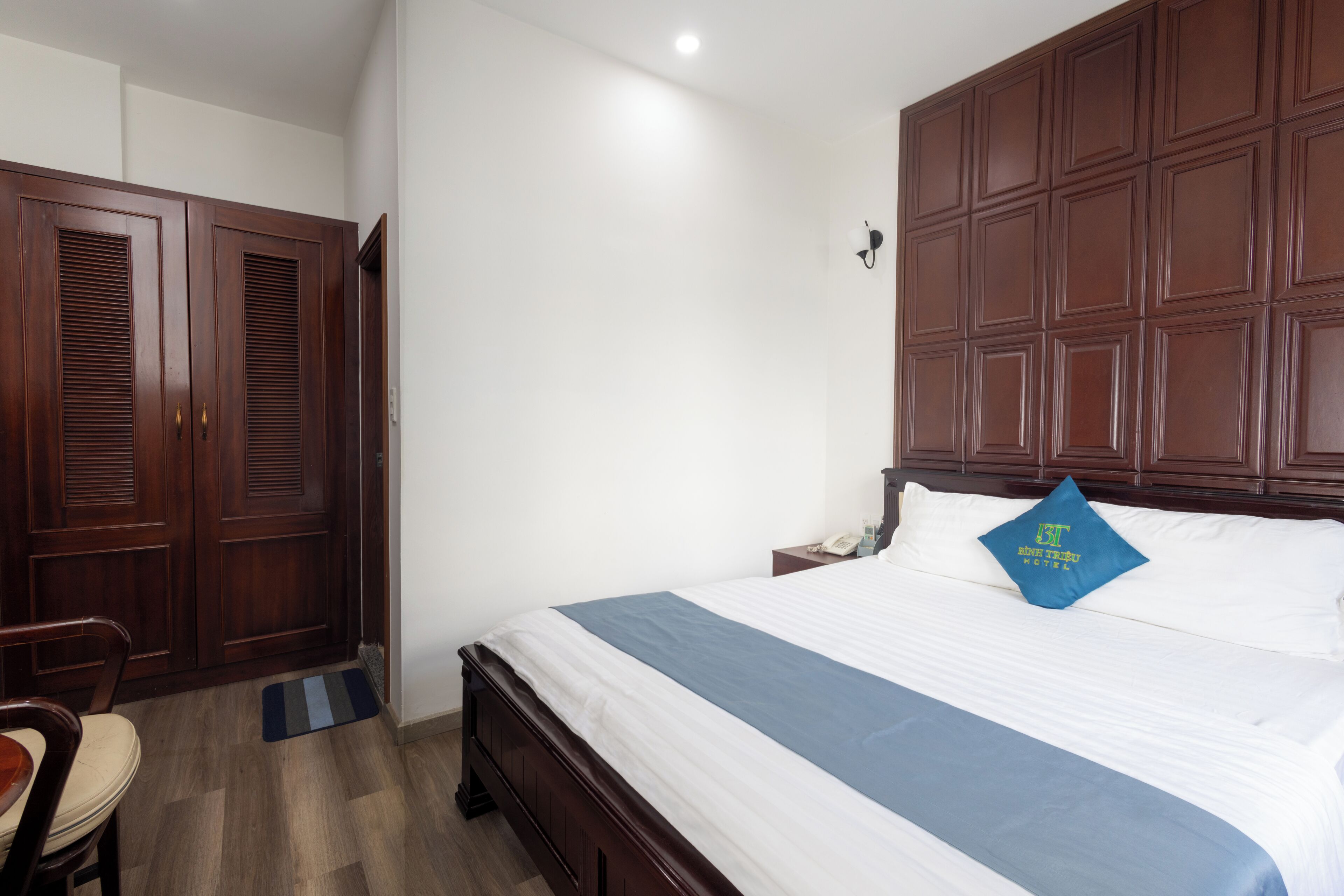A hotel room with a large bed, wooden wardrobe, and a desk with a chair.
