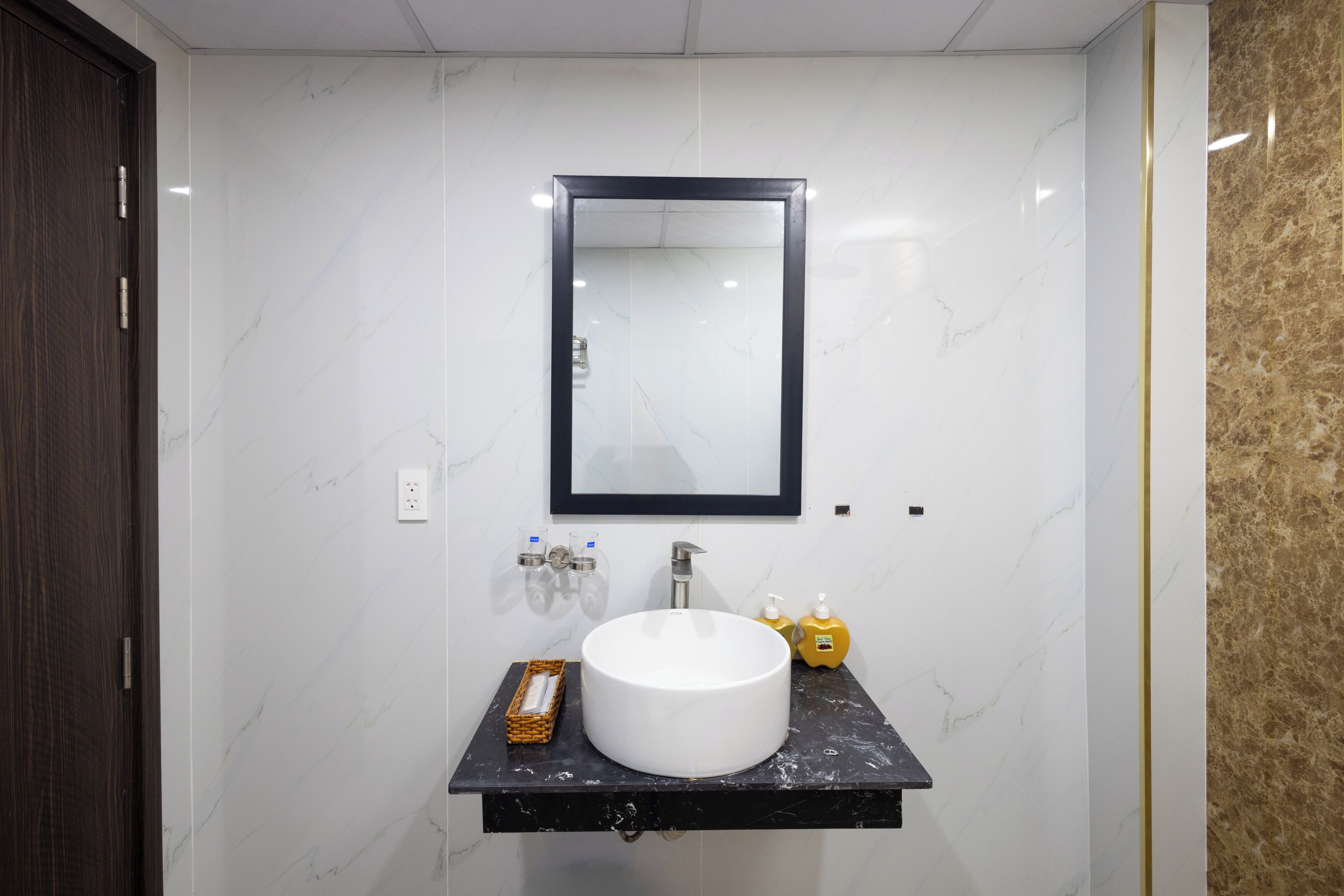 A bathroom with a white marble sink, a black countertop, a mirror, and a gold accent wall.