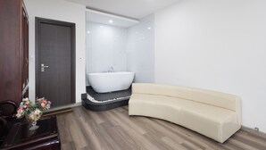 Egy modern fürőszoba, melyben egy különálló, lábakkal rendelkező fürdőkád, egy bézs színű kanapé és egy fa ajtó található.