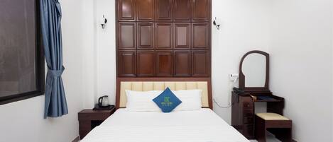 Habitación de hotel con una cama grande, cabecero de madera, mesita de noche con lámpara, un espejo y un escritorio pequeño con una silla.